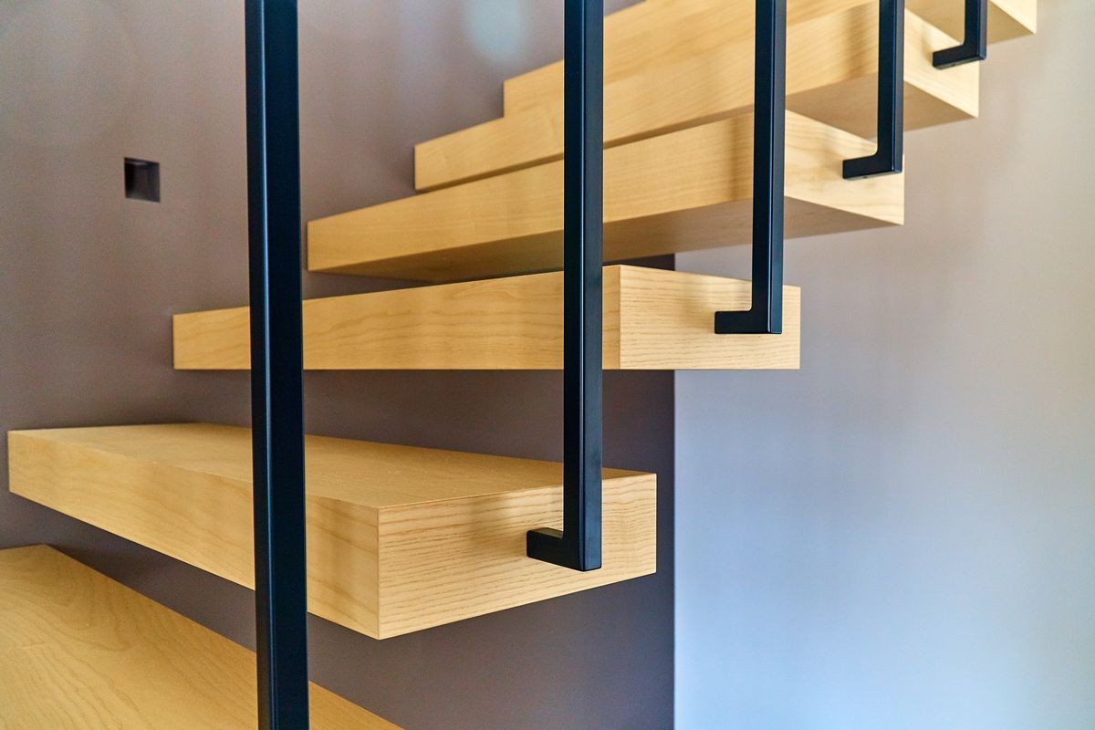 Floating stairs. Ash lumber stairs with railing attached to brown wall and leading to second floor inside stylish modern house